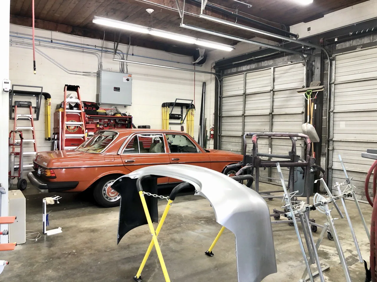 Orange classic car and detached body panel in workshop.