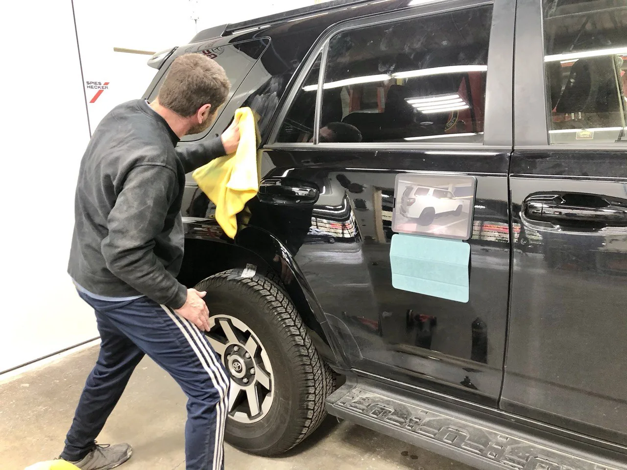 Technician wiping a black minivan with a yellow cloth.