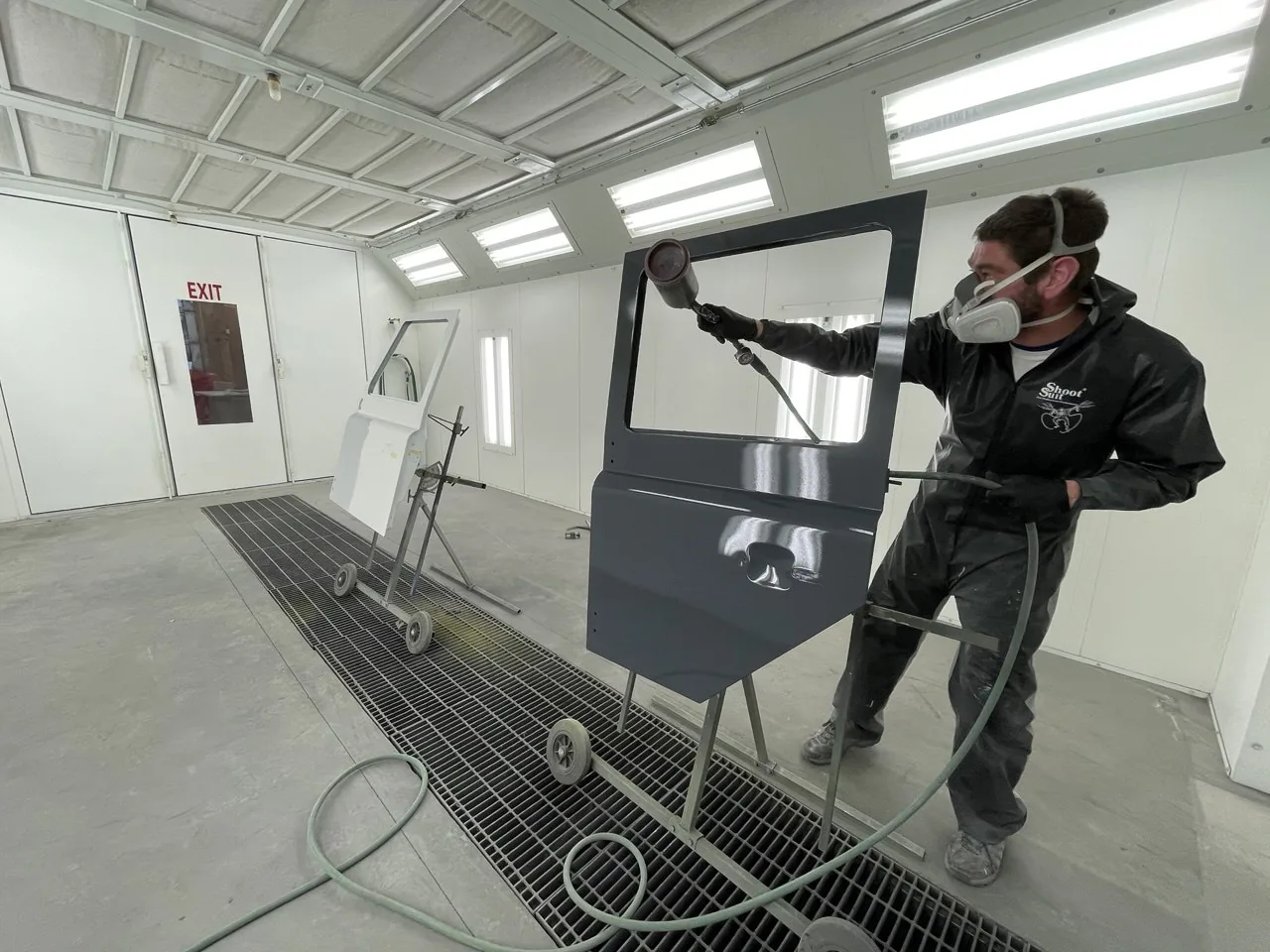 Paint technician spraying a detached body panel in booth.