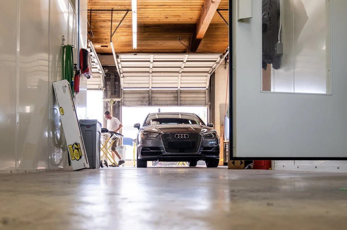 Low-angle view through a workshop bay toward a vehicle and technician.