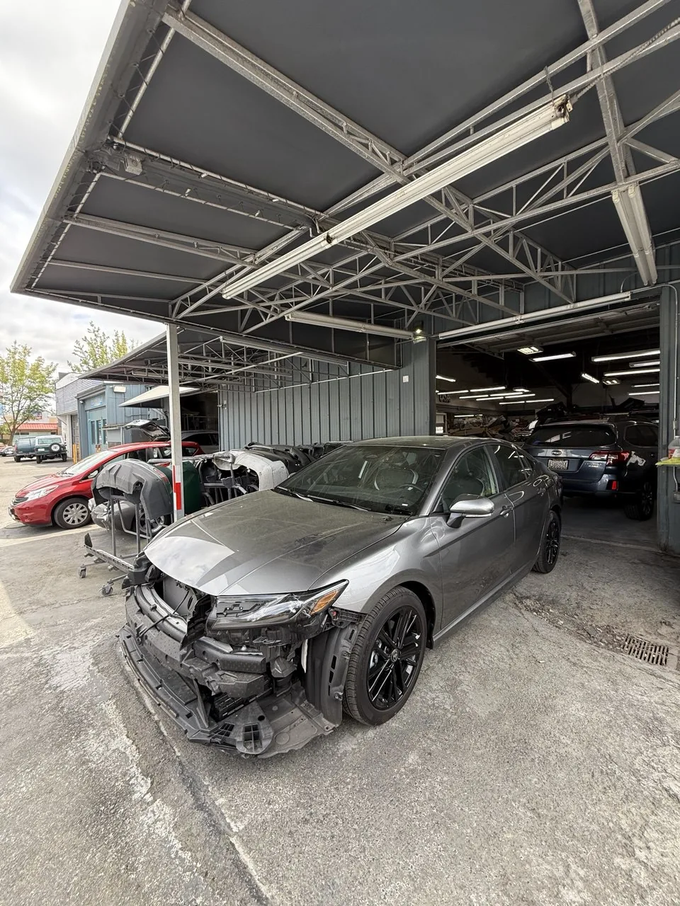 Gray vehicle with front bumper removed in repair bay.
