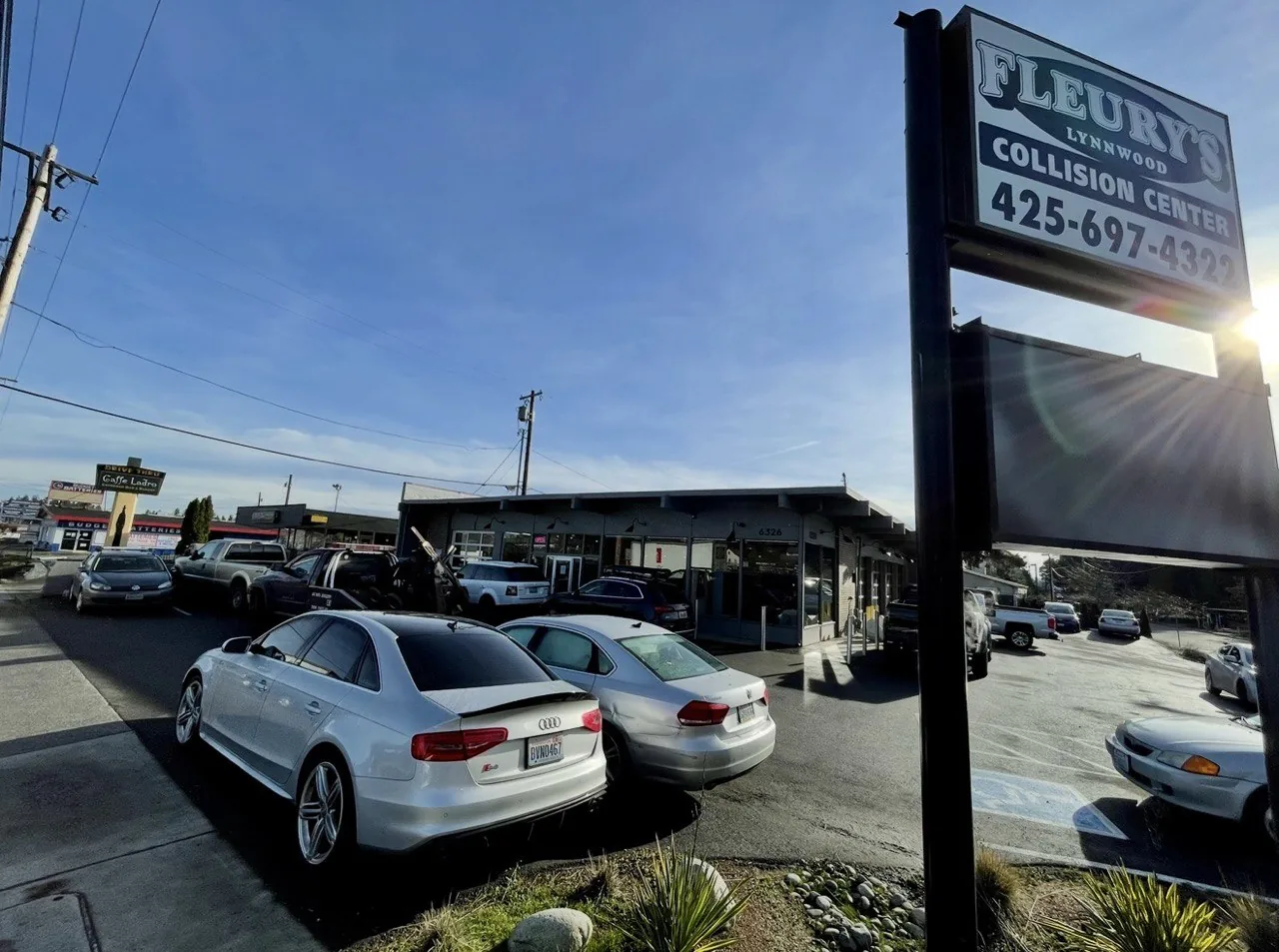 Lynnwood sign and shop exterior with parked cars and sun flare.