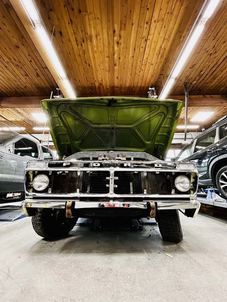 Green classic truck, hood open, inside wood-ceiling workshop.