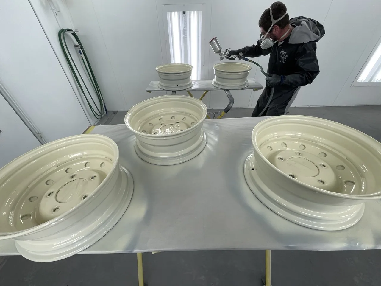 Paint technician spraying white wheels inside booth.