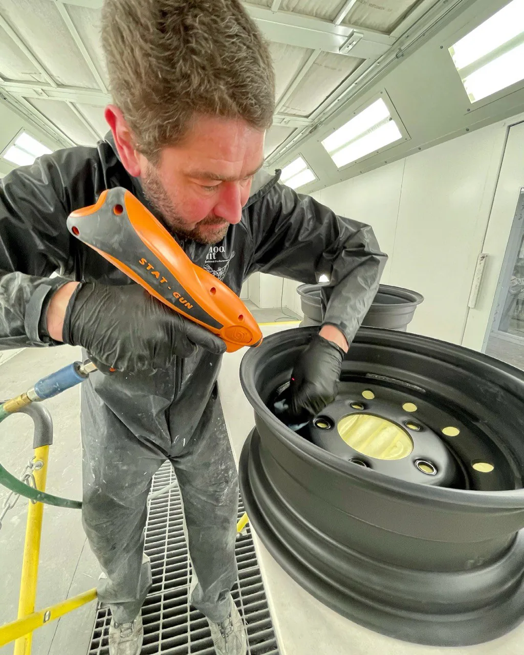 Technician working on a wheel with an antistatic tool in paint booth.