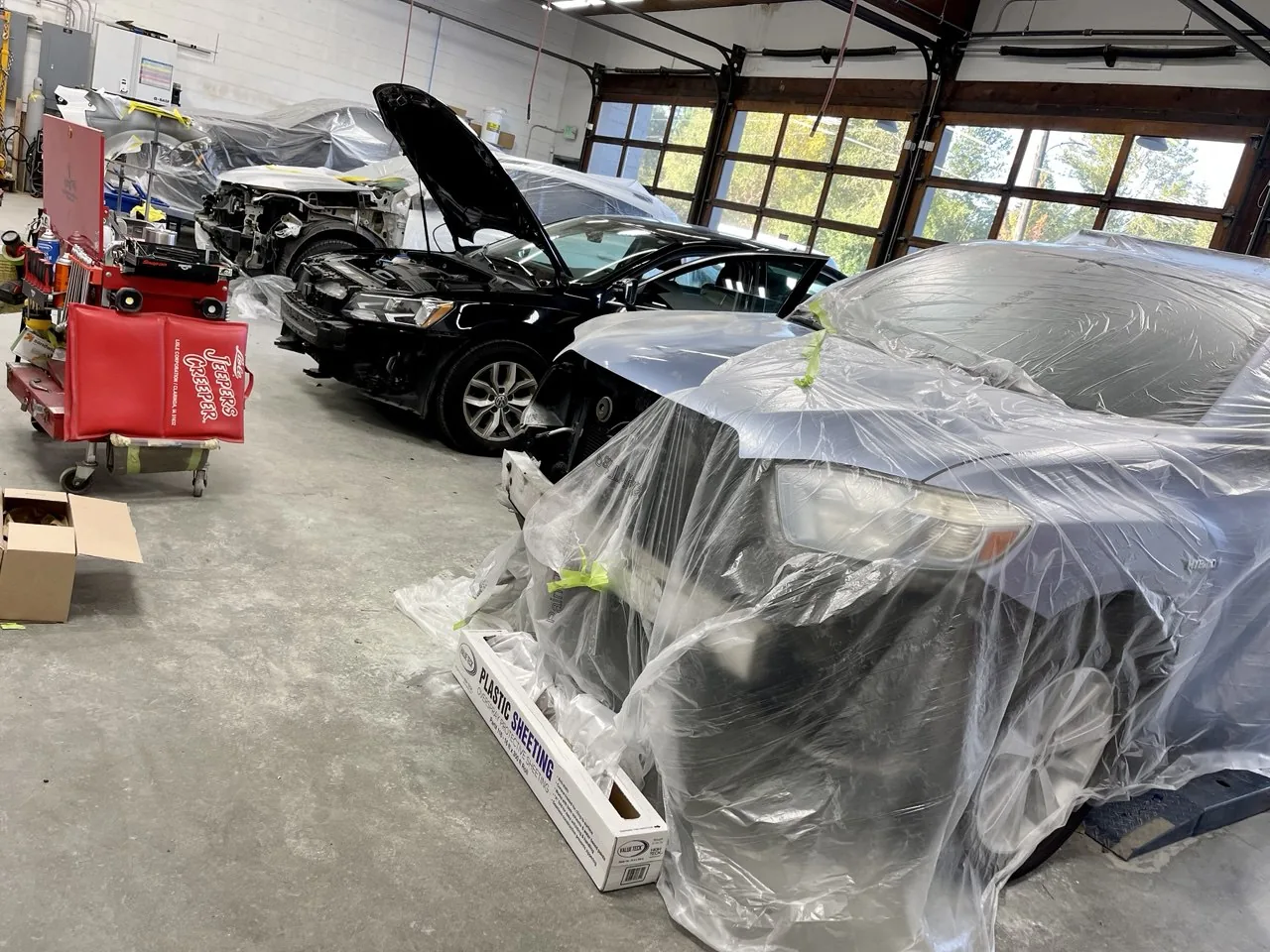 Vehicles covered/masked with protective plastic in workshop.