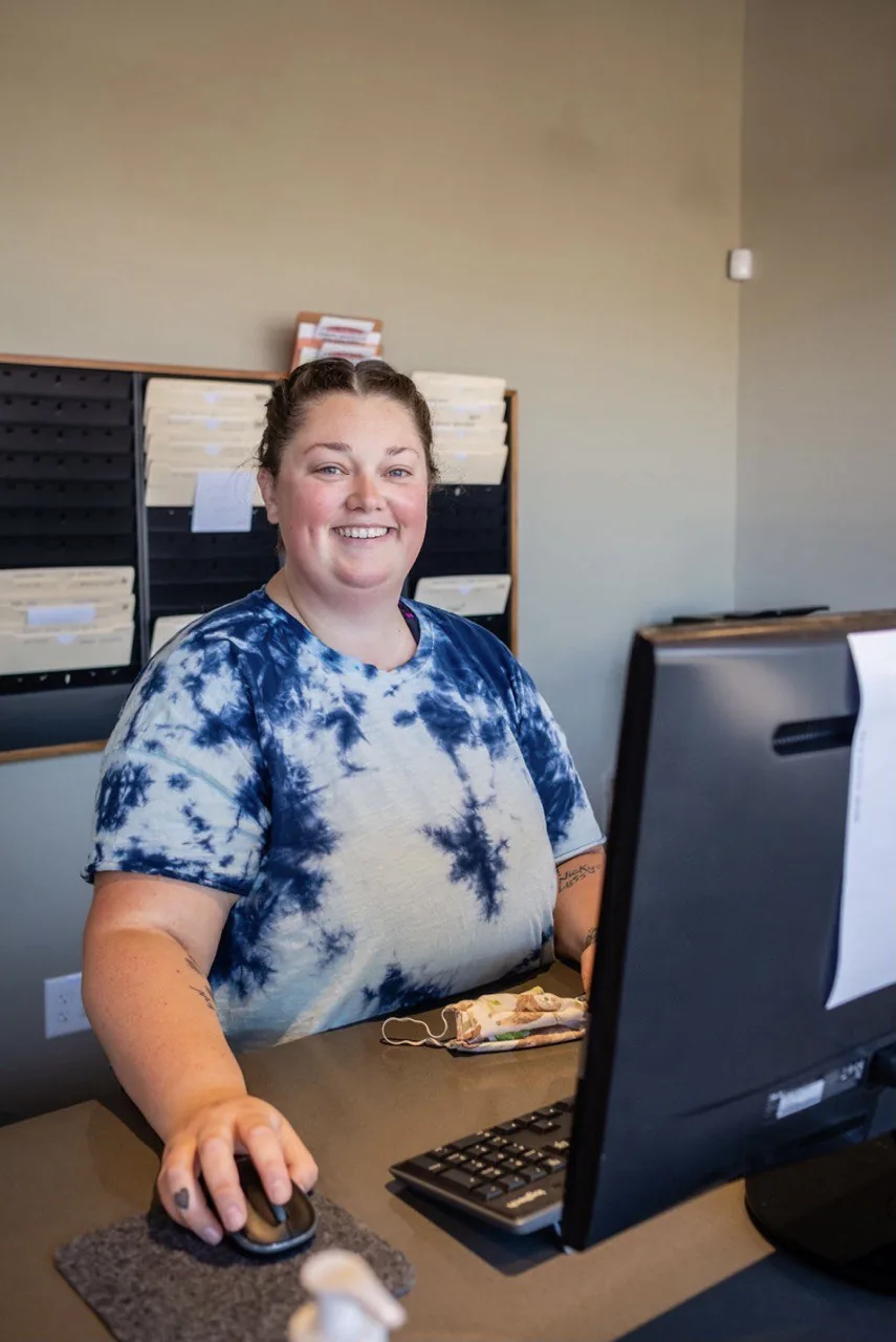 Smiling receptionist at a desk with computer monitors.